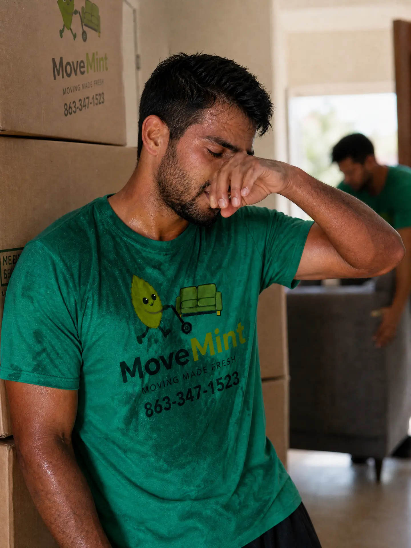 Honest effort on a hot Florida moving day Hardworking MoveMint crew member in a green company shirt wiping his brow beside stacked boxes on a hot Central Florida moving day